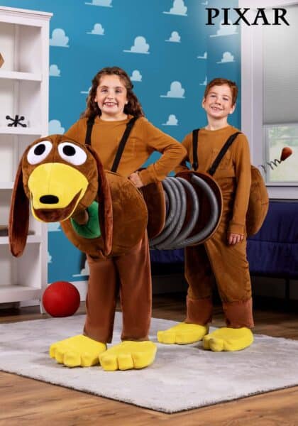 Two children wear a creative Slinky Dog costume from Toy Story, standing together so they form the front and back of the dog, smiling indoors with a PIXAR logo in the top right corner.