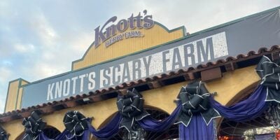 Entrance to Knott’s Scary Farm, decorated with large black bows and purple fabric, featuring a sign with the event’s name under the Knott’s Berry Farm logo.
