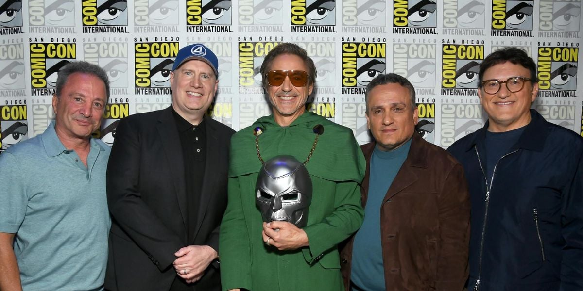 Five men, including Robert Downey Jr., stand together smiling at San Diego Comic-Con in front of a Comic-Con International step-and-repeat backdrop; the center man holds a Doctor Doom mask.
