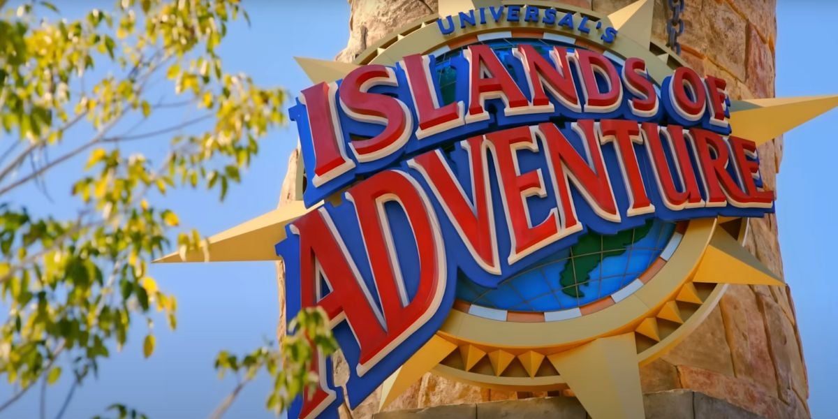 A colorful sign reading “Universal’s Islands of Adventure” is mounted on a stone pillar, with blue sky and green tree leaves in the background—home to thrilling attractions like Spider-Man.