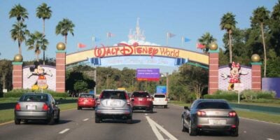 Cars drive toward the colorful Disney World entrance arch, featuring images of Mickey and Minnie Mouse.