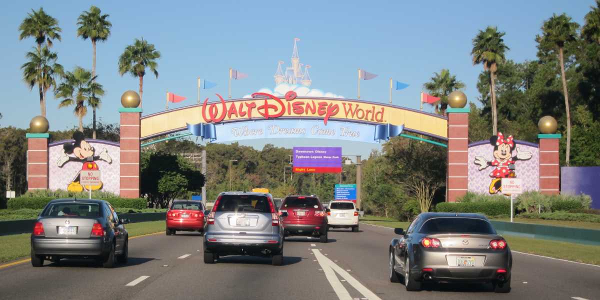 Cars drive toward the colorful Disney World entrance arch, featuring images of Mickey and Minnie Mouse.