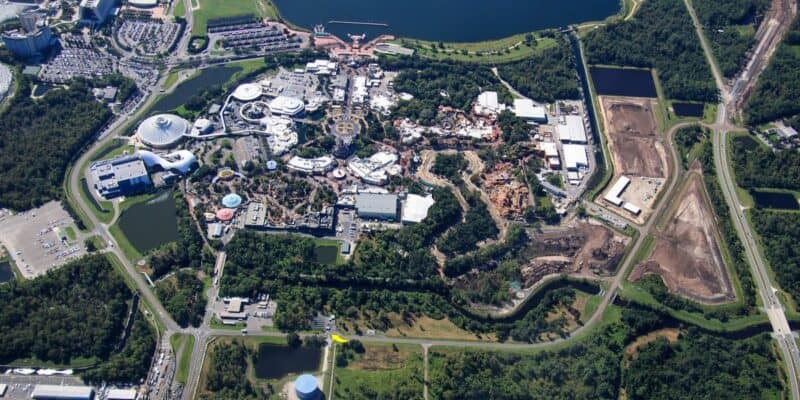 Aerial view of a large theme park complex surrounded by trees, roads, and parking lots, with various buildings, rides, and water areas visible within the park.