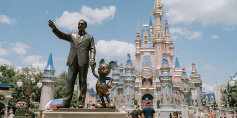 A bronze statue of Walt Disney holding Mickey Mouse’s hand in front of Cinderella Castle in Disney World