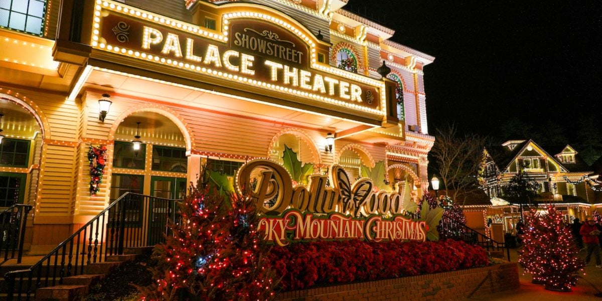 The Dollywood Palace Theater, inspired by Dolly Parton, is brightly lit at night with festive holiday lights and decorations, red Christmas trees, and a sign reading “Dollywood Smoky Mountain Christmas.”.