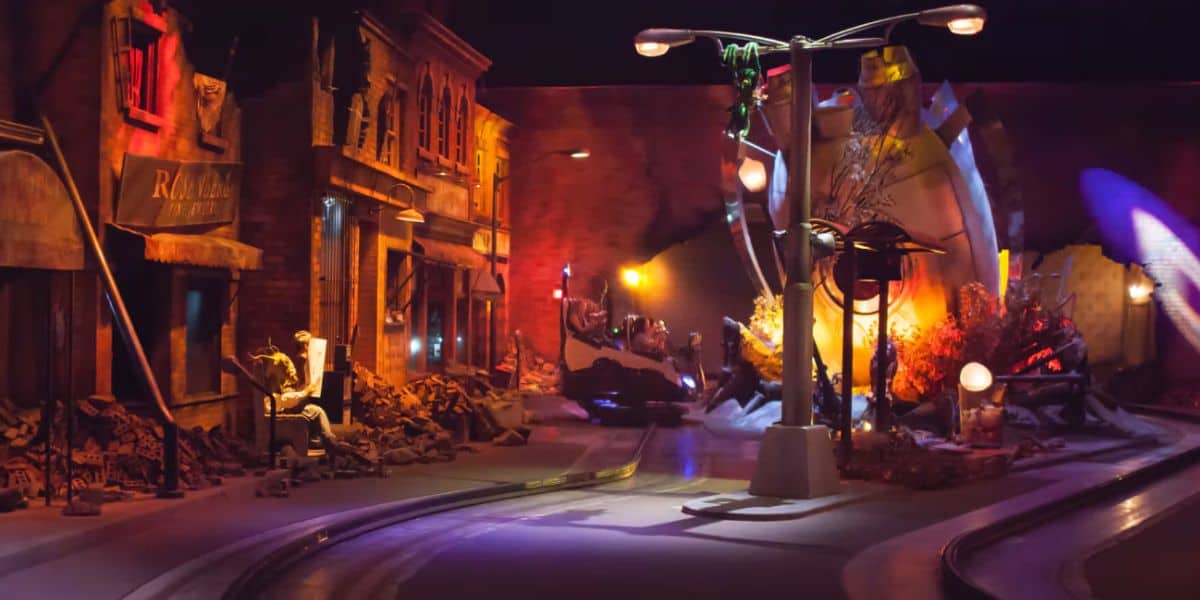 A dimly lit theme park ride simulates a city street scene with damaged buildings, scattered debris, and dramatic lighting, creating an atmosphere of destruction and chaos—like a Men in Black mission in the midst of alien attack.