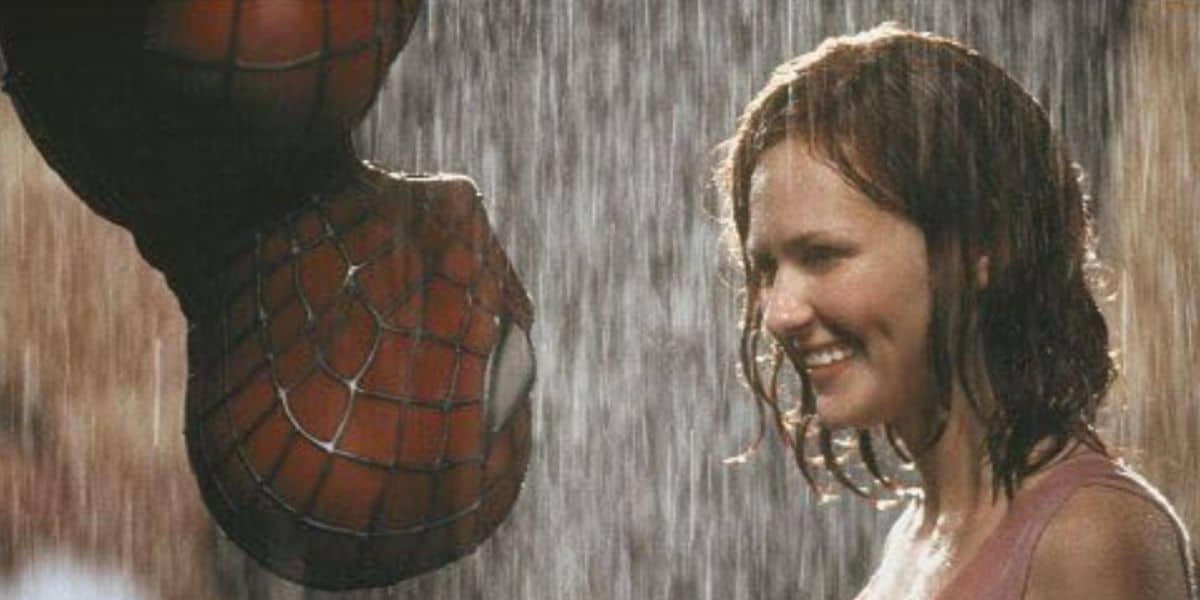 A person in a spider-man costume hangs upside down in the rain, facing a smiling woman with wet hair. They appear to be about to share an iconic Spider-Man kiss.