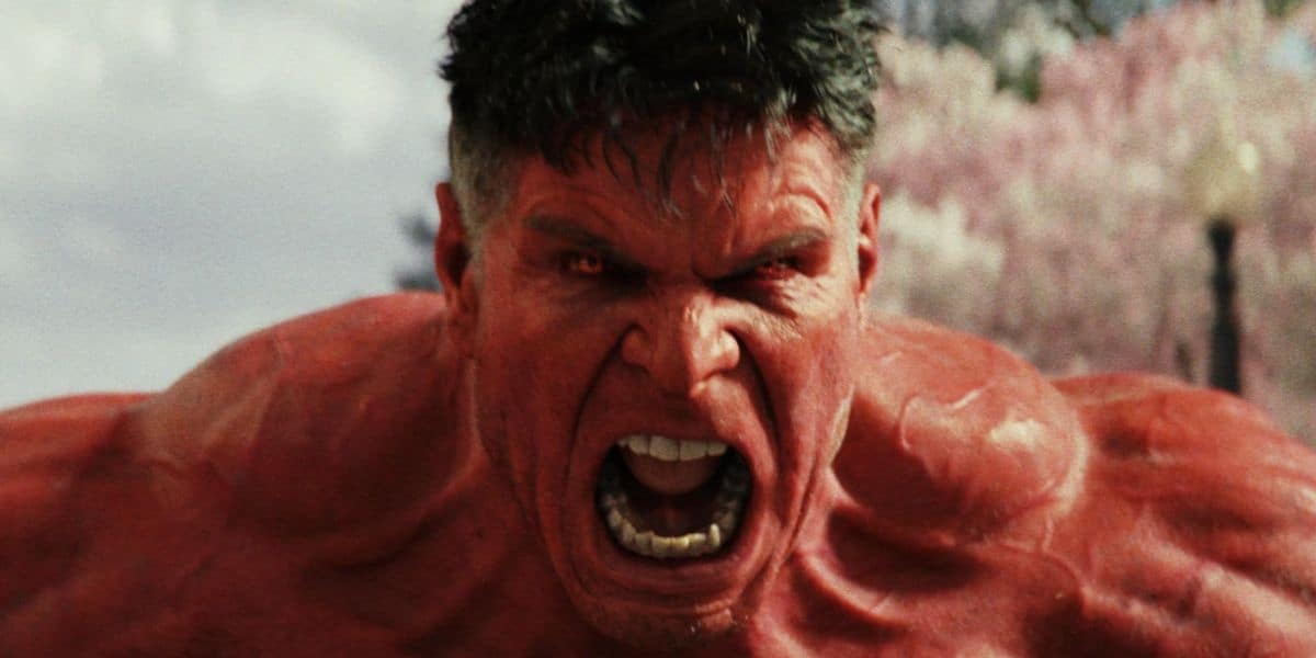 A muscular, red-skinned character with short dark hair and glowing red eyes roars angrily, baring teeth—reminiscent of a furious Captain America. The background is slightly blurred with pinkish trees and a cloudy sky.