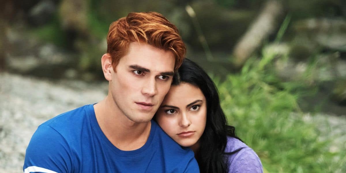 A young man with red hair in a blue shirt sits beside a young woman with long dark hair in a purple top, who rests her head on his shoulder. They both look serious and pensive, as if reflecting on the recent cancellation of the Riverdale franchise.