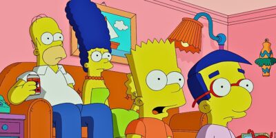Homer, Marge, Bart, and Milhouse from 'The Simpsons' sit on a couch in the living room, looking surprised at something off-screen.