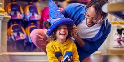 Man puts a Sorcerer Mickey hat on a child at Disney