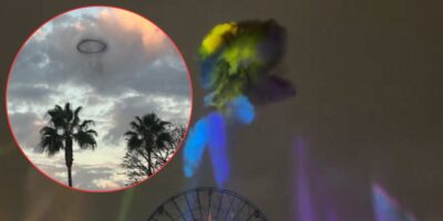 A dark ring-shaped cloud floating above palm trees and a ferris wheel in a cloudy sky, with colorful lights beaming upward.