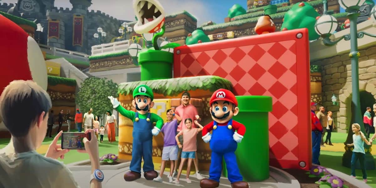 People take photos with costumed characters Luigi and Mario at a colorful, Super Mario-themed amusement park at Universal, featuring green pipes, a Piranha Plant, and vibrant decorations inspired by the video game.