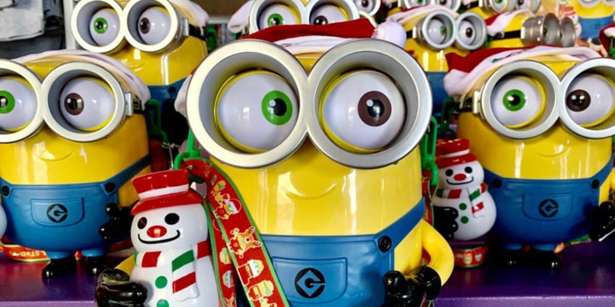 Several Universal Minion toys dressed in Santa hats are grouped together. The central Minion holds a festive snowman figure and wears a holiday-themed ribbon, creating a cheerful universal holiday display.