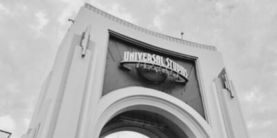 A black and white photo of the entrance archway to Universal Orlando, featuring the large iconic sign set against dramatic, ghostly clouds swirling in the sky above.