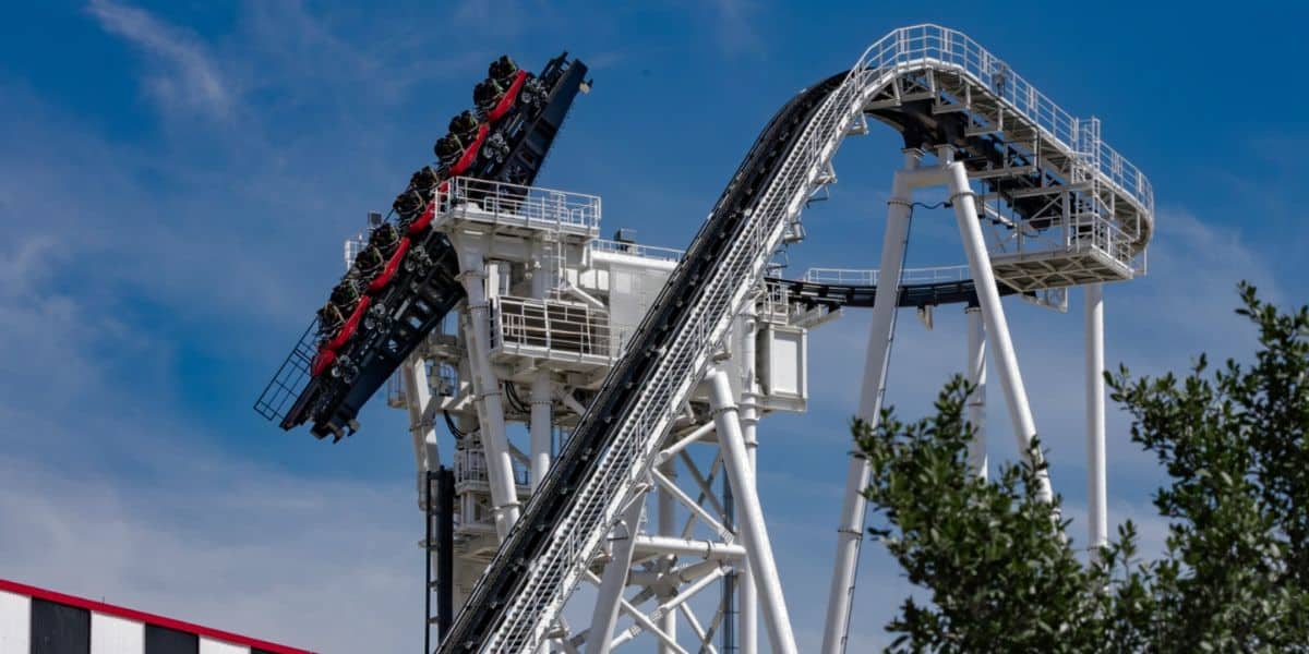 Thrill-seekers hang vertically on the Intimidator 305’s steep ascent, their excitement sky-high against a clear blue backdrop.