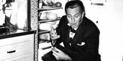 A dapper Disney historian sits by an open fridge, animatedly recounting stories of Walt and his legendary $9M housekeeper legacy.
