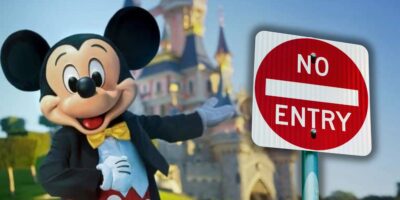 Mickey Mouse stands in front of Cinderella Castle at Disneyland Paris, showing just how packed this Disney park can get during the Holidays, playfully pointing to a "No Entry" sign near the entrance.