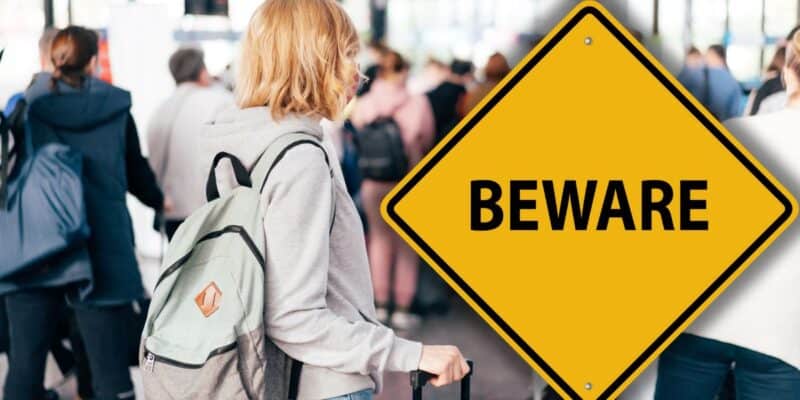 A guest with a backpack navigates the bustling park crowd near a prominent yellow "BEWARE" sign, adding to the thrill as Disney World and Universal Orlando guests attempt to either fly home or fly into their theme parks through January 4, 2026.