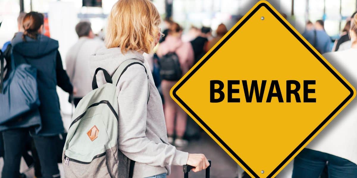 A guest with a backpack navigates the bustling park crowd near a prominent yellow "BEWARE" sign, adding to the thrill as Disney World and Universal Orlando guests attempt to either fly home or fly into their theme parks through January 4, 2026.