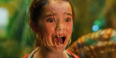 A Jurassic World Rebirth guest with a frightened look sports part-reptile features: scaly skin and sharp teeth.