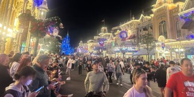 Guests fill Main Street, U.S.A. under twinkling lights at night, with Cinderella Castle brilliantly illuminated in the background.