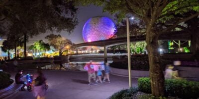 Spaceship Earth glows purple at night as guests walk by the Monorail tracks.