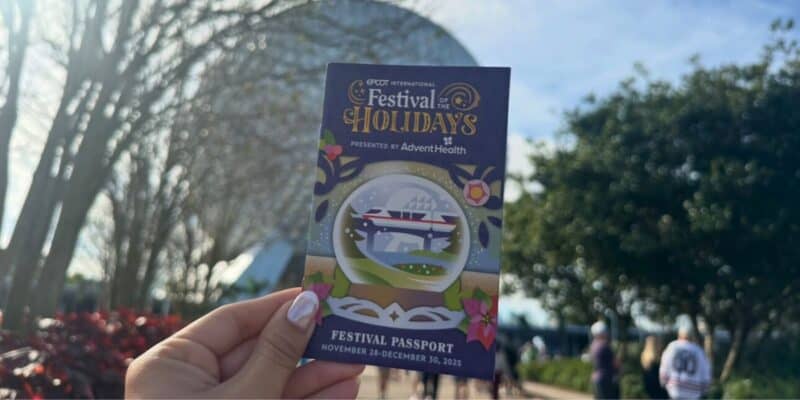 EPCOT Festival of the Holidays passport held up in front of Spaceship Earth, ready for park hopping and festive fun.