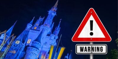 A caution sign stands near Cinderella Castle at night inside of Disney World, illuminated by dazzling lights in the heart of Magic Kingdom.