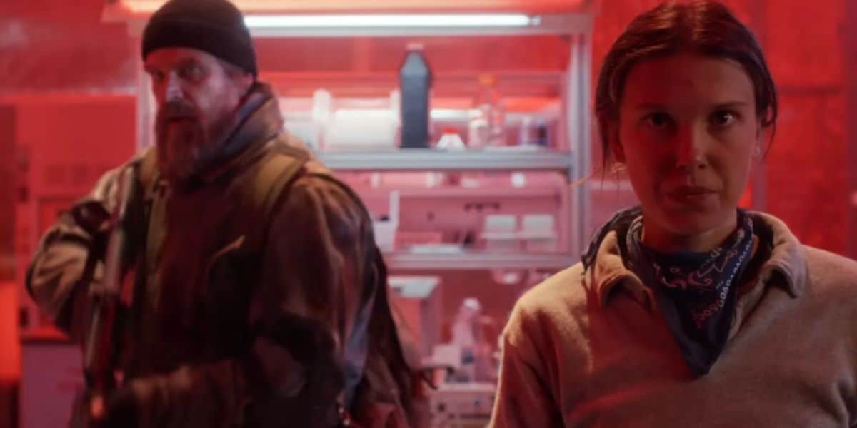 A young woman explores a sci-fi lab, while a rugged explorer stands behind her, all illuminated by vibrant red show lights.