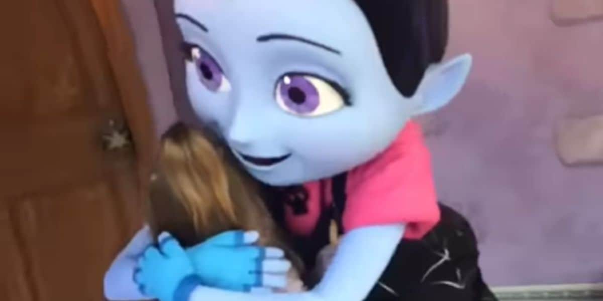 A child hugs a Disney character performer dressed as Vampirina.