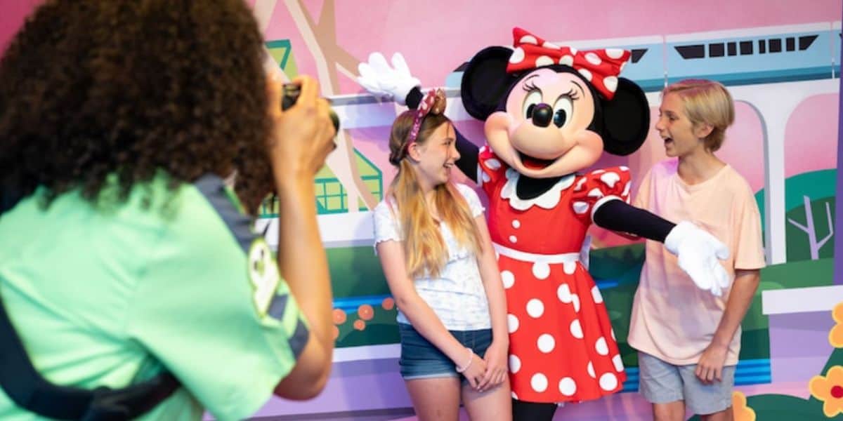 two younger guests take a picture with Minnie Mouse against a backdrop with the monorail on it