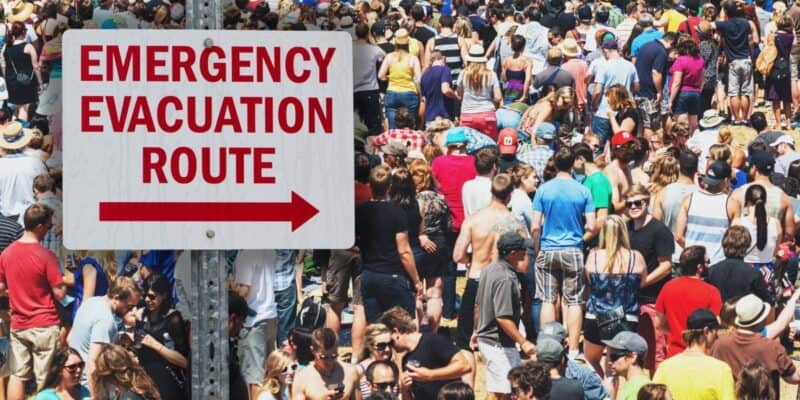 Guests navigate a bustling Disney World Resort hotel area after news breaks out of an evacuation underway due to a possible dangerous situation as the Emergency Evacuation Route sign directs visitors toward the right.