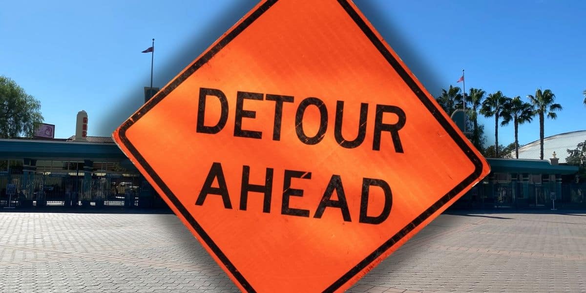 Orange "Detour Ahead" sign stands in front of an empty Disney California Adventure plaza lined with palm trees and attraction buildings inside of Disneyland Resort.
