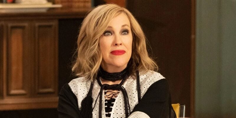 A stylish woman with wavy blond hair and red lipstick poses indoors, channeling old Hollywood glam in black and white attire.