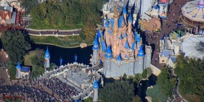 Aerial shot of Cinderella Castle with blue spires, bustling guests, and lush trees at Magic Kingdom in Walt Disney World.