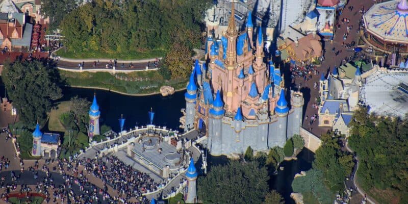 Aerial shot of Cinderella Castle with blue spires, bustling guests, and lush trees at Magic Kingdom in Walt Disney World.