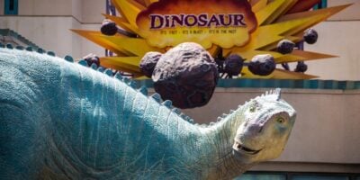The Dino Institute’s iconic dinosaur statue stands before the DINOSAUR ride sign in Disney's Animal Kingdom Theme Park at Walt Disney World Resort.