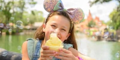 disney kid wearing sparkling Mickey Ears headband holds a cup of dole whip in front of Big Thunder Mountain