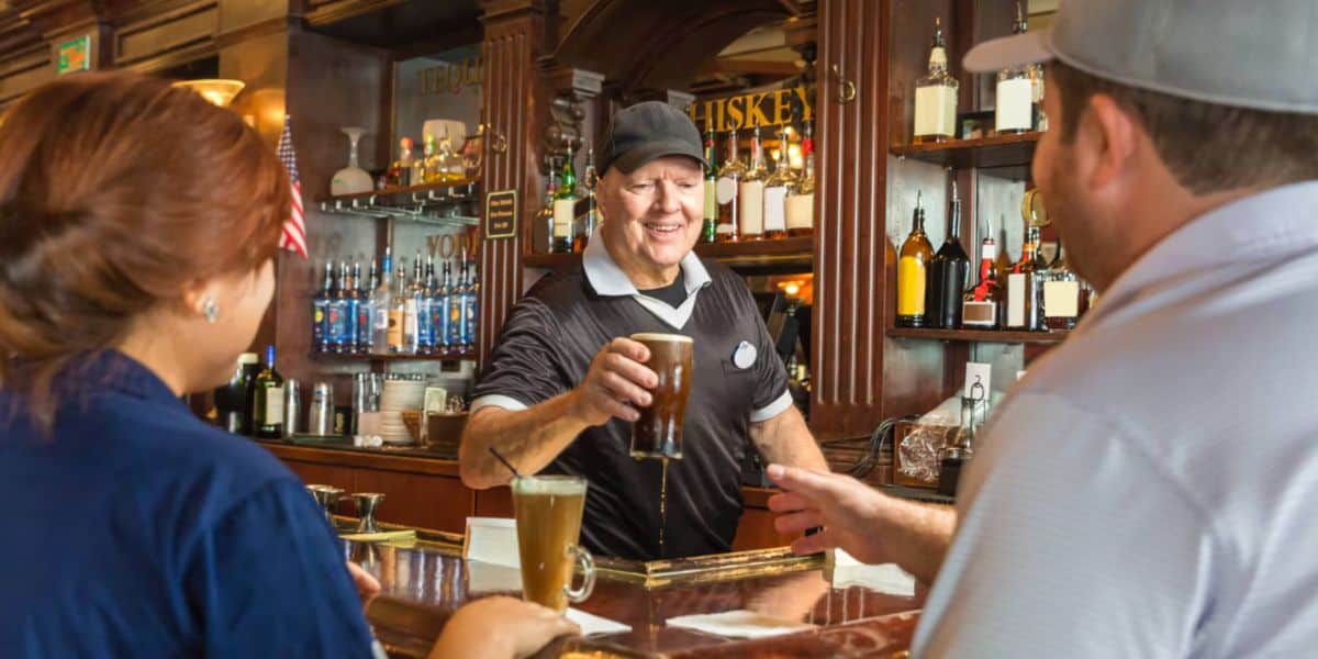 A friendly bartender at Universal’s iconic bar serves drinks to guests, with shelves of themed bottles lining the lively backdrop.