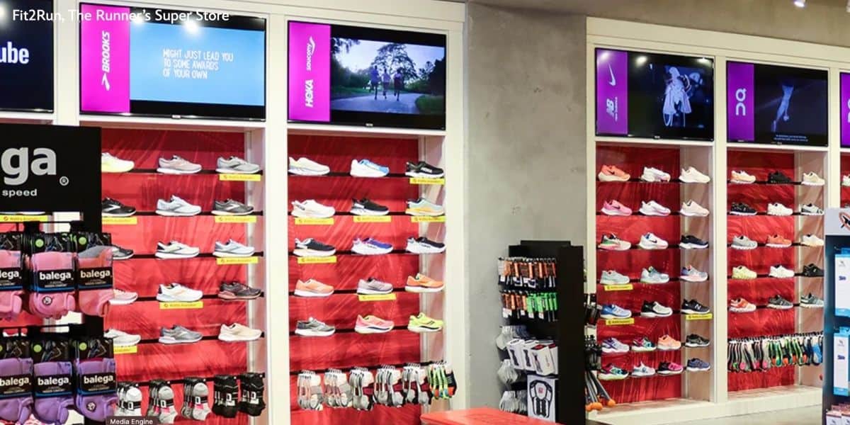 A vibrant wall of running shoes and socks with animated ads overhead, evoking classic Disney Store magic before it closed.