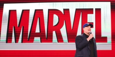 Kevin Feige takes the stage in his signature blue cap, addressing fans with Marvel’s iconic red logo glowing behind him.
