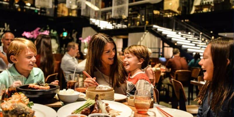 A family shares laughs around a colorful Disney Springs restaurant table filled with themed dishes and fun drinks.