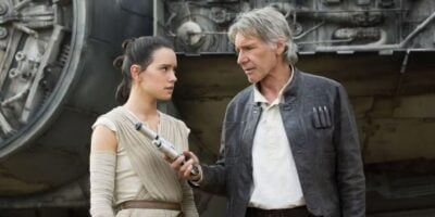 Han (Harrison Ford) hands a lightsaber to Rey (Daisy Ridley) outside the Millennium Falcon