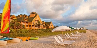 Colorful seaside resort with sunny yellow buildings, beach lounges, umbrellas, and kayaks—evoking classic Disney vacation magic.