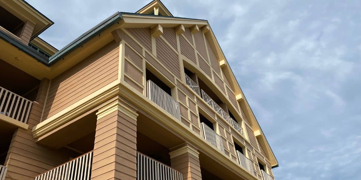 A multi-story tan hotel with balconies and cream trim at Disney’s Forgotten Resort, seen from below against a cloudy sky.