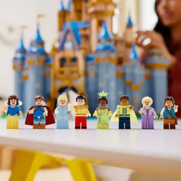 Seven beloved Disney princesses and princes pose by a blue and gold LEGO Disney Castle.