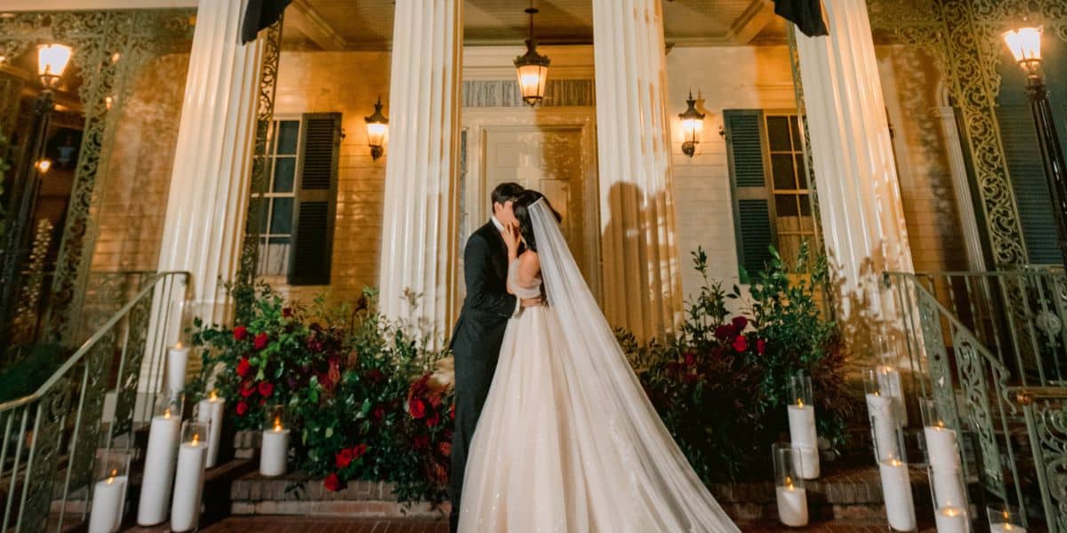 Newlyweds kiss at night before the Haunted Mansion, aglow with themed floral and candlelight decor, capturing Disney magic.