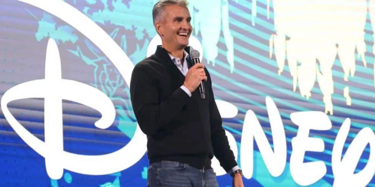 Josh D'Amaro on stage with "Disney" written in bright white letters on the screen behind him