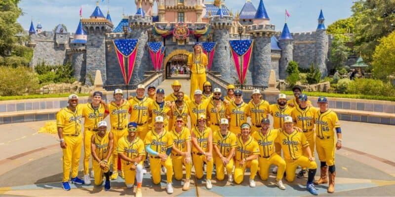 A baseball team in bright yellow uniforms poses at Magic Kingdom before Cinderella Castle, festooned with American flags.